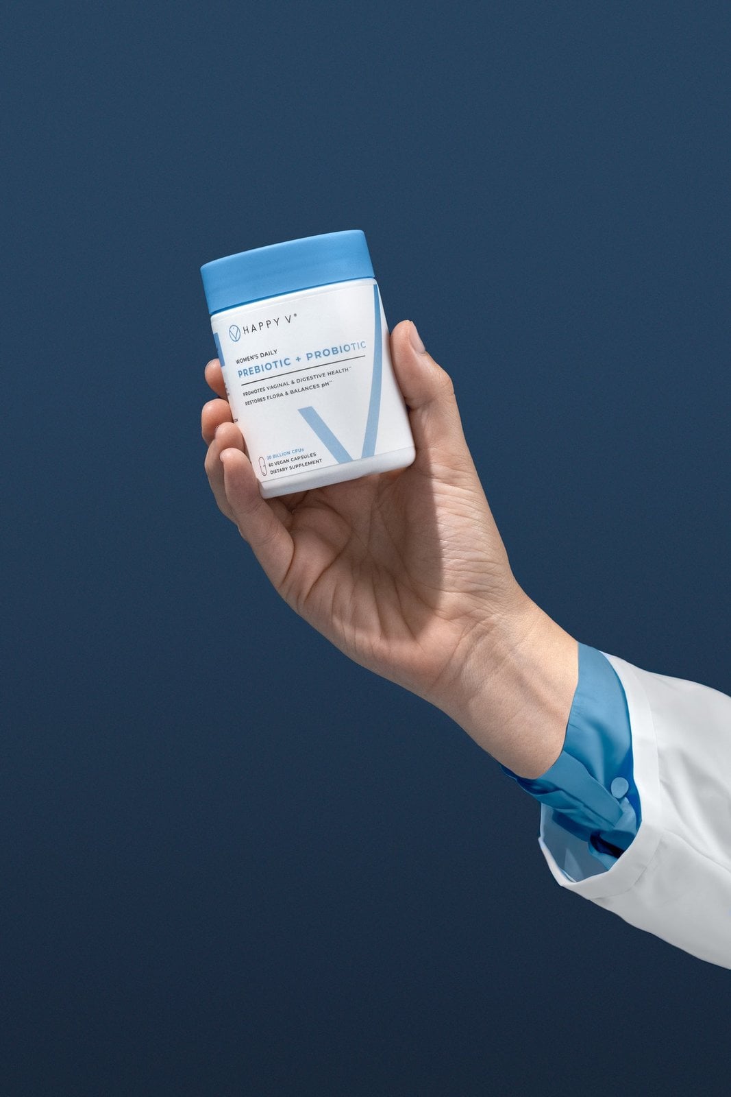 A hand holding a Happy V probiotic bottle against a blue background