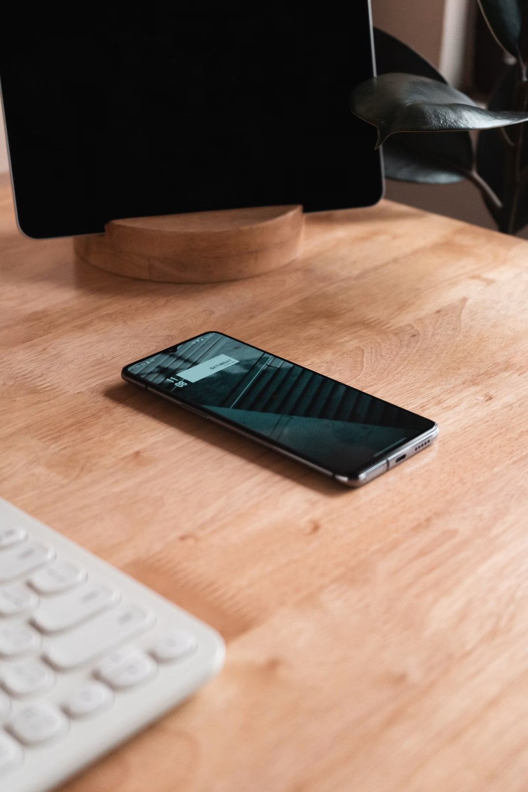 Smartphone resting on a wooden desk beside a keyboard