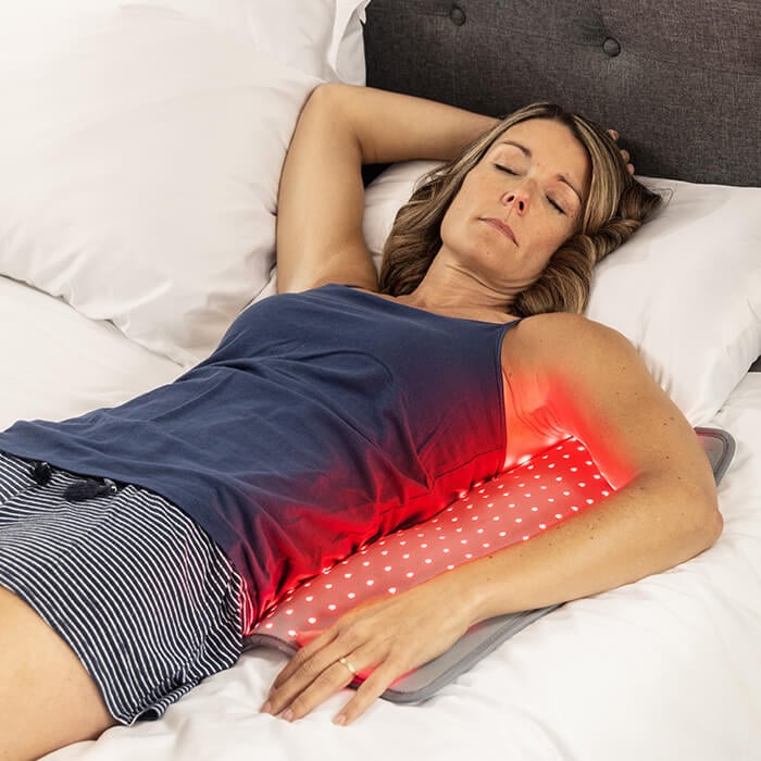 A person positioning a red light therapy pad