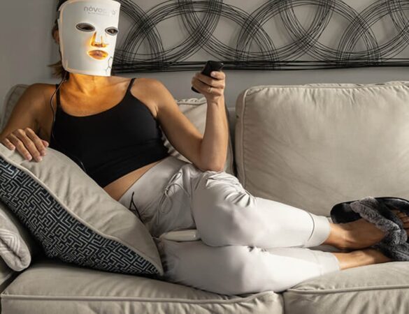 Person reclining on a sofa wearing a red light therapy mask