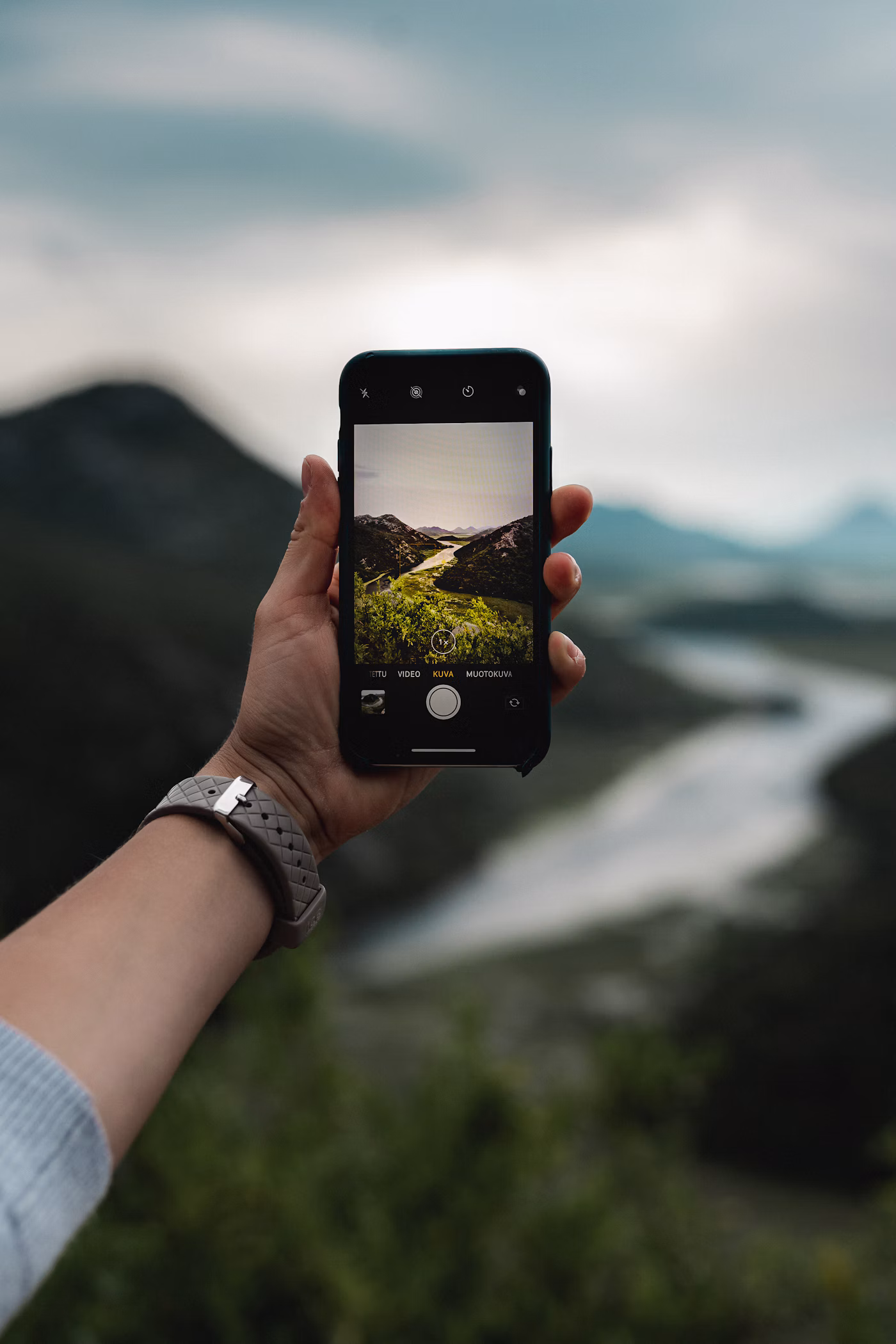 Person holding a smartphone while photographing a lakeside view